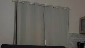 Moderni olohuone, jossa on tummanharmaa sohva, pyöreä puinen sohvapöytä sekä keittiöalue, jonka taustaseinässä on laattaa ja jossa on puiset kaapit.