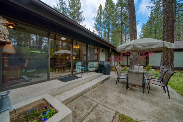 A covered patio with outdoor furniture, a concrete planter with flowers, and a view of the surrounding forest.