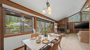 A dining area with a long table set for six, a fireplace, and a TV in a living room area. - Pet friendly, fully fenced, A/C (Graeagle)