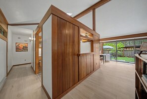 A room with wooden paneling, a sliding door, a dining area with outdoor seating, and a view of the backyard.