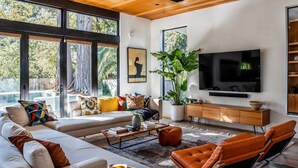 A modern living room with a large TV, comfortable seating, and a large window.