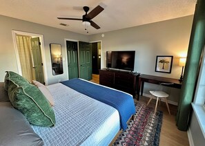 Habitación de hotel con dos camas, un escritorio, un televisor y un ventilador de techo.