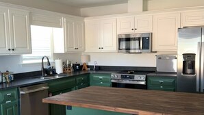 Una cocina moderna con armarios verdes, una isla de madera con taburetes, electrodomésticos de acero inoxidable y una lámpara en el techo.