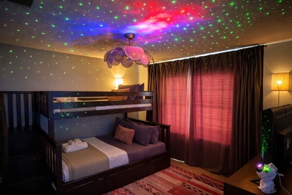 A room with a bunk bed, a desk with a computer, and a ceiling with star-like lights.
