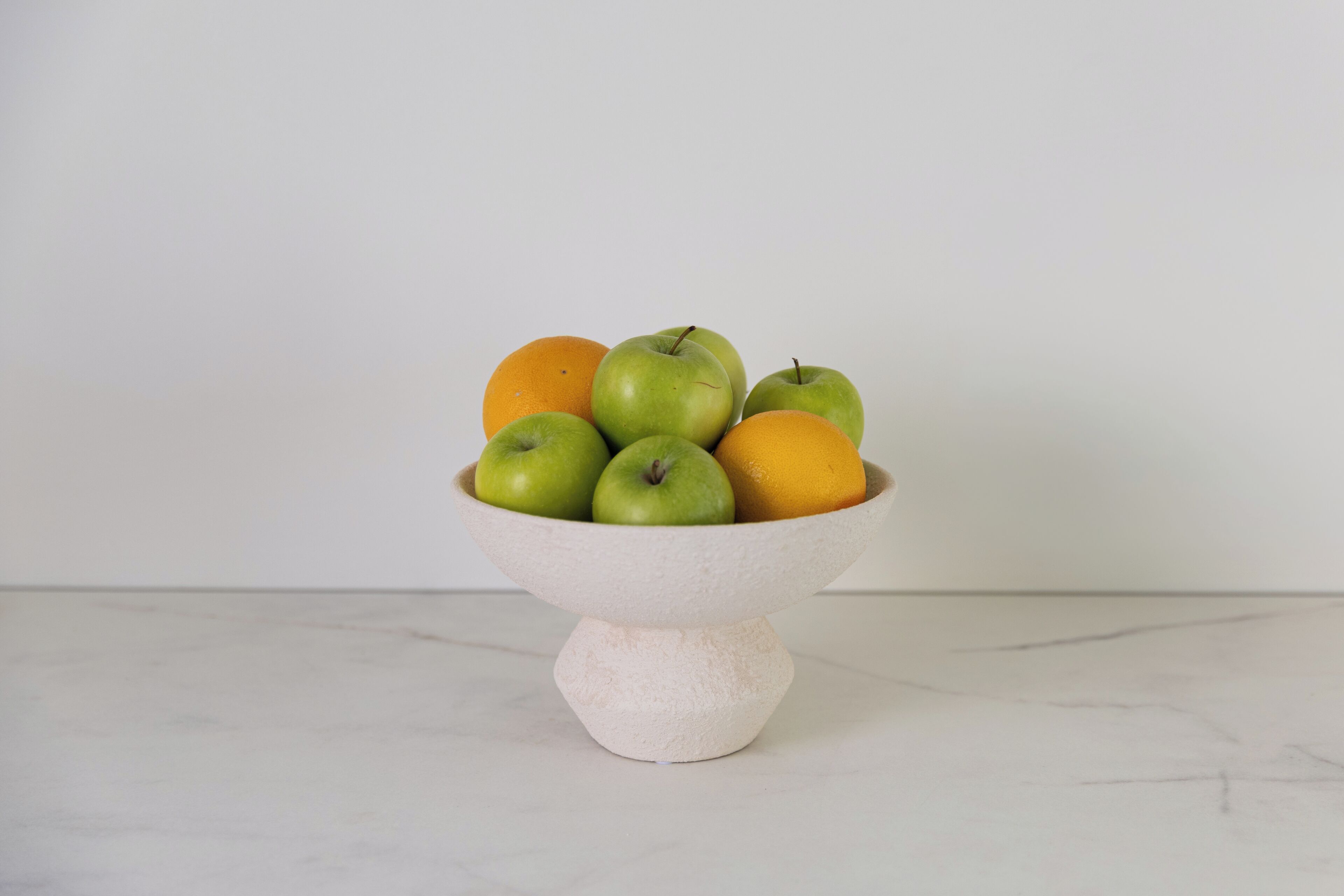 A bowl of fruit on a marble surface.