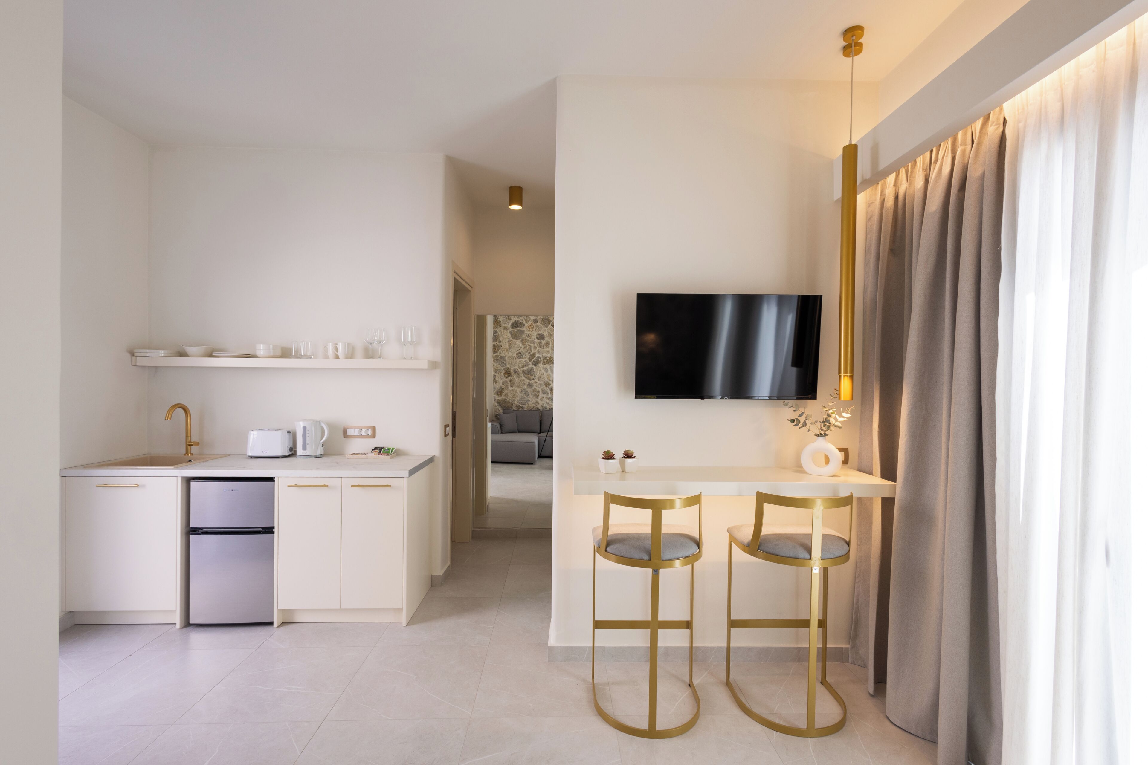 A modern kitchen with a built-in dishwasher, a white countertop, and a TV mounted above a bar area with two stools.