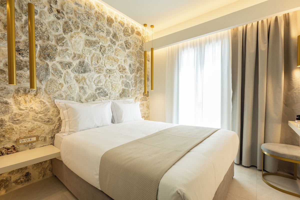 A bed with white bedding, a stone wall, and a window with curtains.
