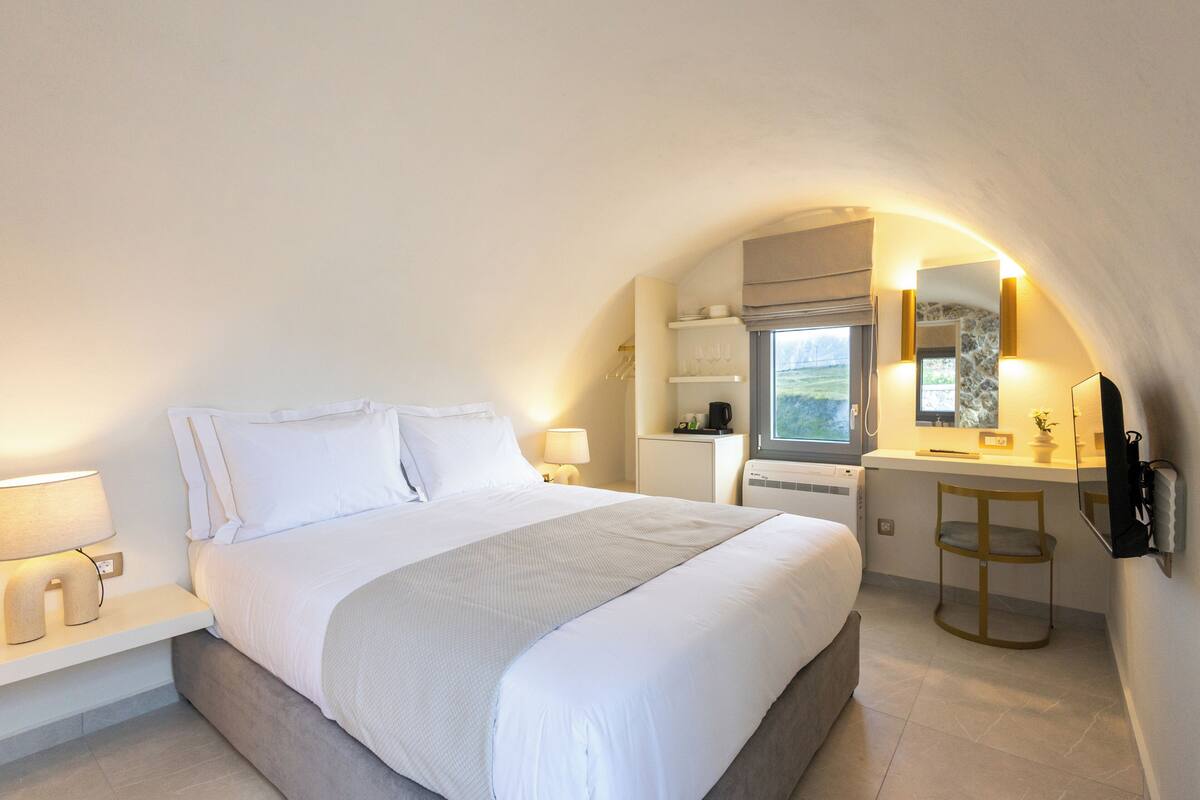 A bedroom with a bed, bedside table, lamp, and a small desk with a chair.