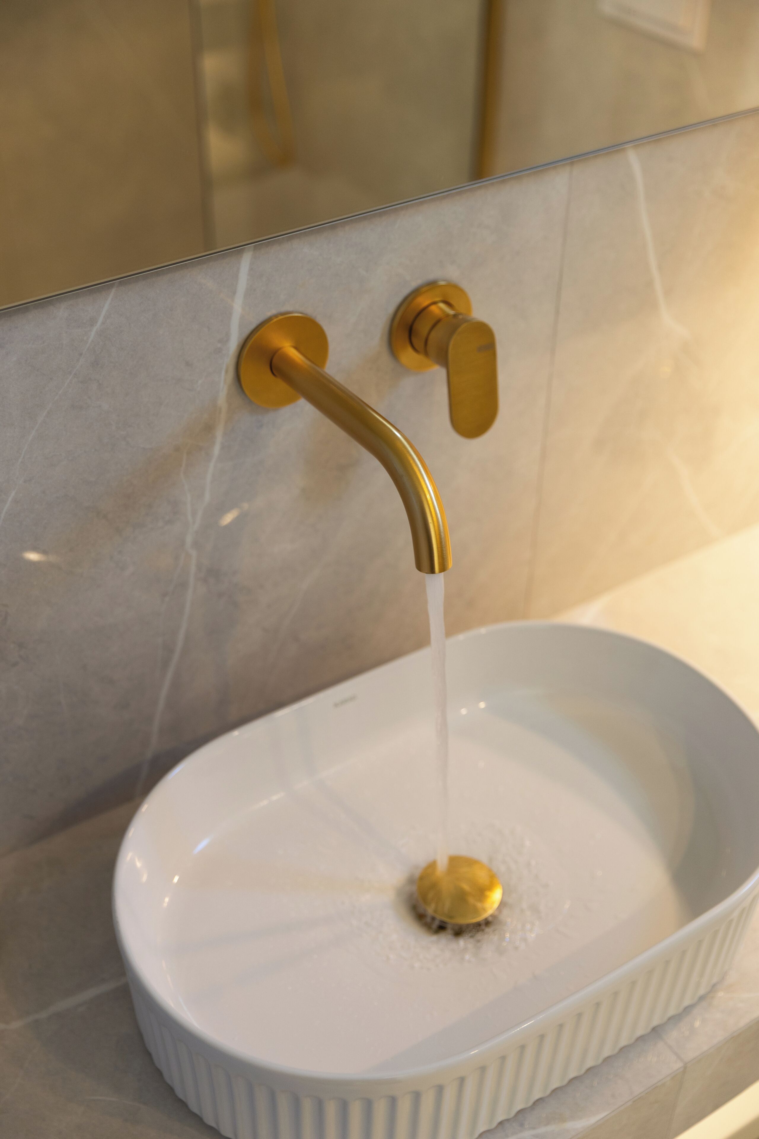 A bathroom with a white sink, gold faucet, and marble tiles.