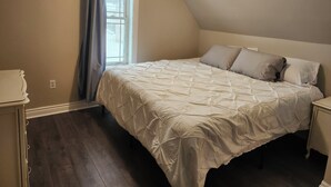 A bedroom with a bed, a window with curtains, a bedside table, and a dresser. - Cozy Brockville Getaway | Walk to River, Dining & Downtown (Brockville)
