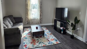 A living room with a sofa, a coffee table, a TV, and a potted plant. - Cozy Brockville Getaway | Walk to River, Dining & Downtown (Brockville)