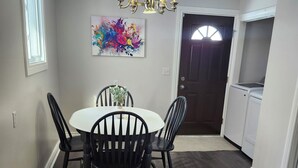 A dining area with a round table and six chairs, a chandelier, and a colorful abstract painting on the wall. - Cozy Brockville Getaway | Walk to River, Dining & Downtown (Brockville)