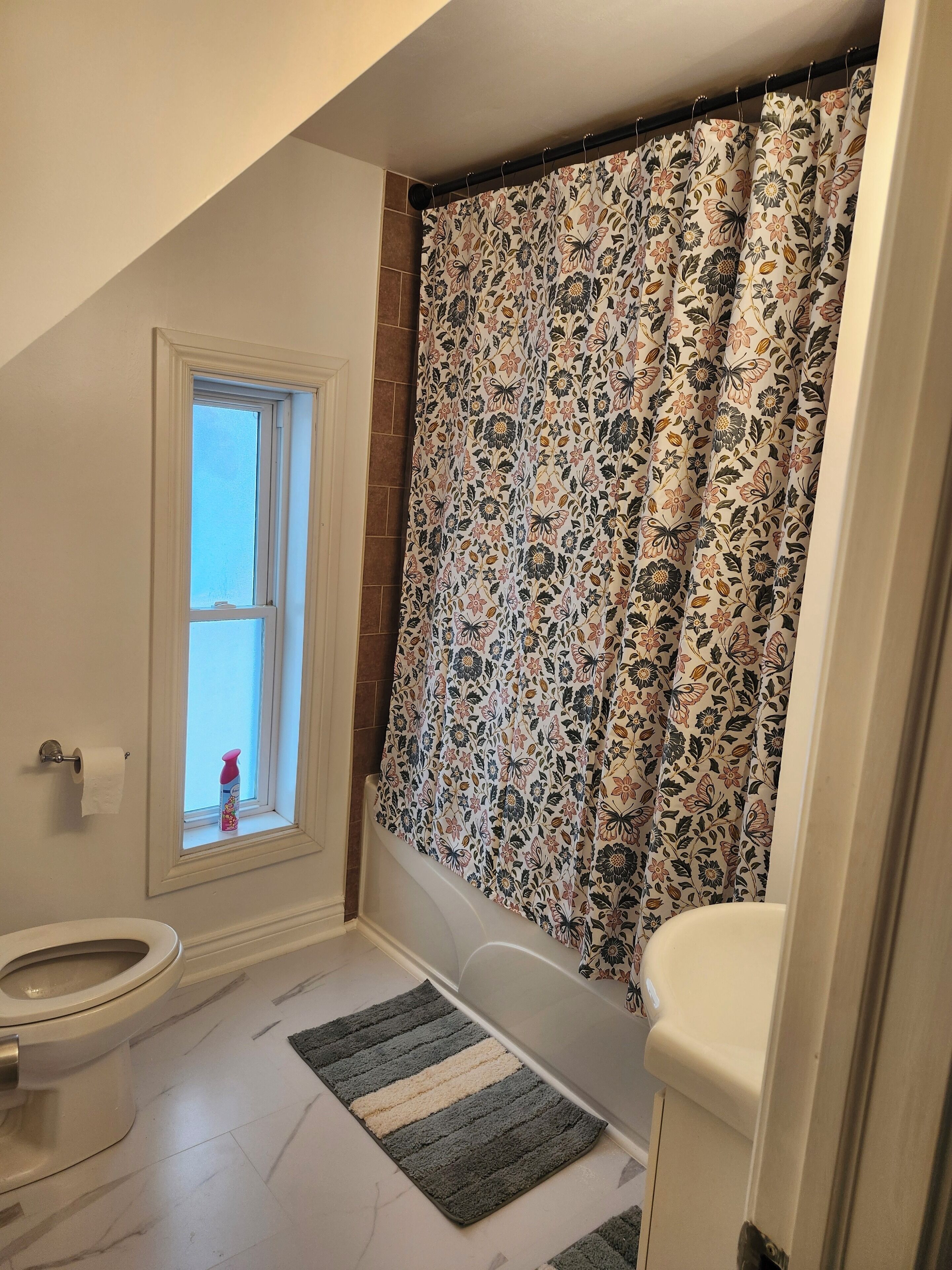 Un baño con inodoro, ventana, cortina de ducha y felpudo.
