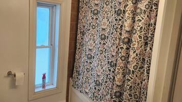 Un baño con inodoro, ventana, cortina de ducha y felpudo.