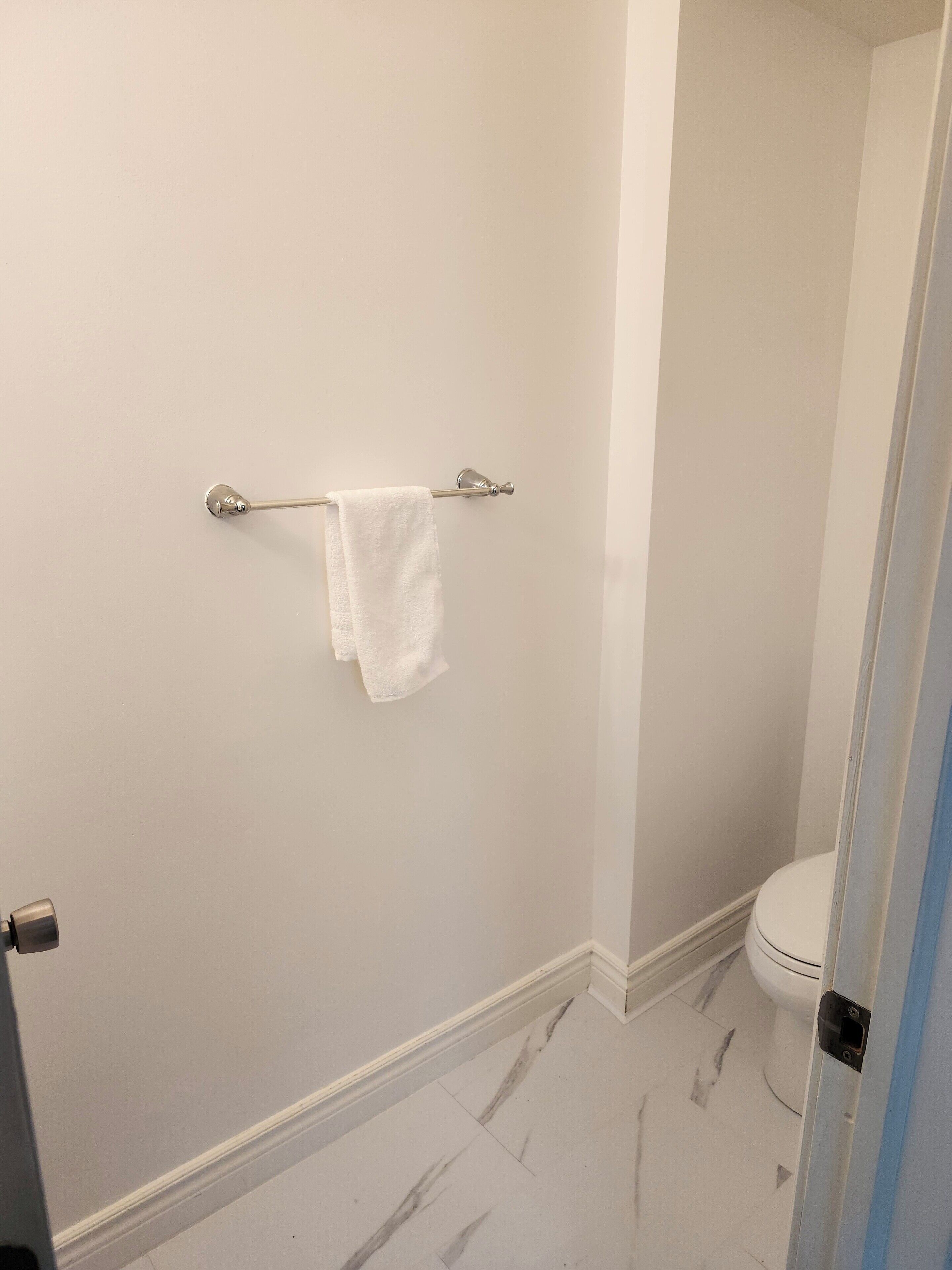Een badkamer met een wit toilet, een handdoek aan een metalen handdoekhouder en een marmeren vloer.