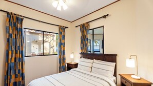 Quarto com cama, cortinas, mesa de cabeceira com abajur e janela com vista.