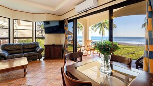 Sala de estar com televisão, sofá, mesa de jantar e vista para o oceano.