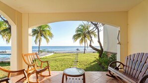 Um pátio com vista para a praia, móveis de madeira e palmeiras.