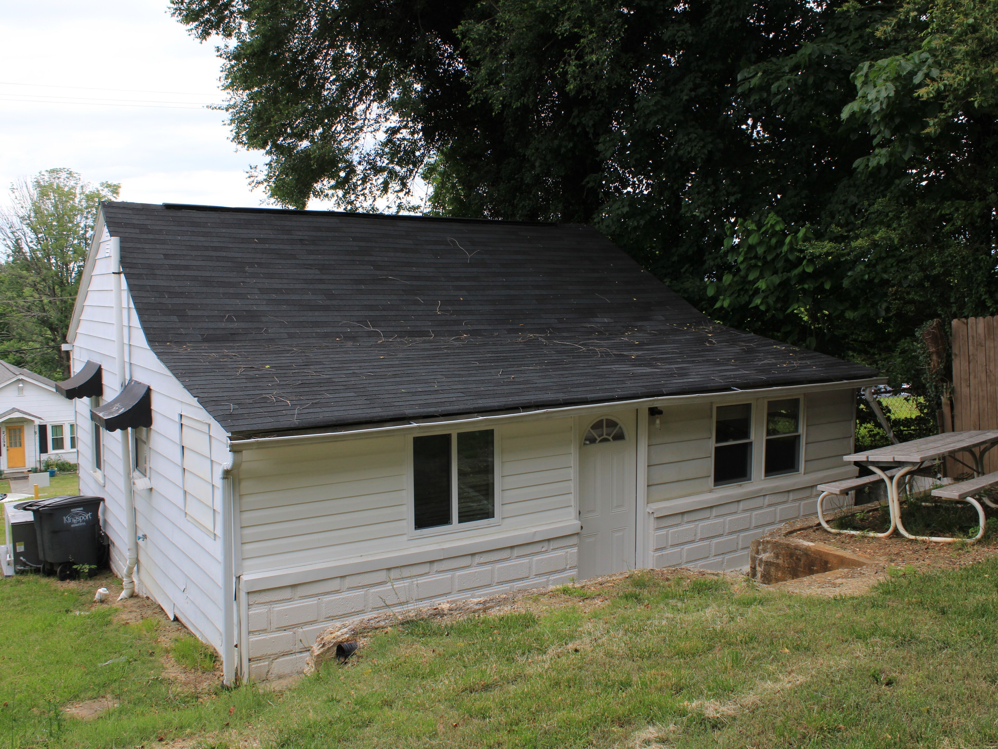 A small, single-story house with a dark shingled roof, a front door, and a small porch area.
