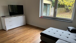 A bedroom with a bed, a TV on a dresser, and a window with a view of a garden. - Sindel Living Apartment-Freshly renovated 2-bedroom apartment with floor heating (Sindelfingen)
