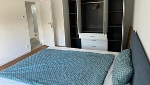 A bedroom with a bed, a wardrobe, and a door leading to another room. - Sindel Living Apartment-Freshly renovated 2-bedroom apartment with floor heating (Sindelfingen)