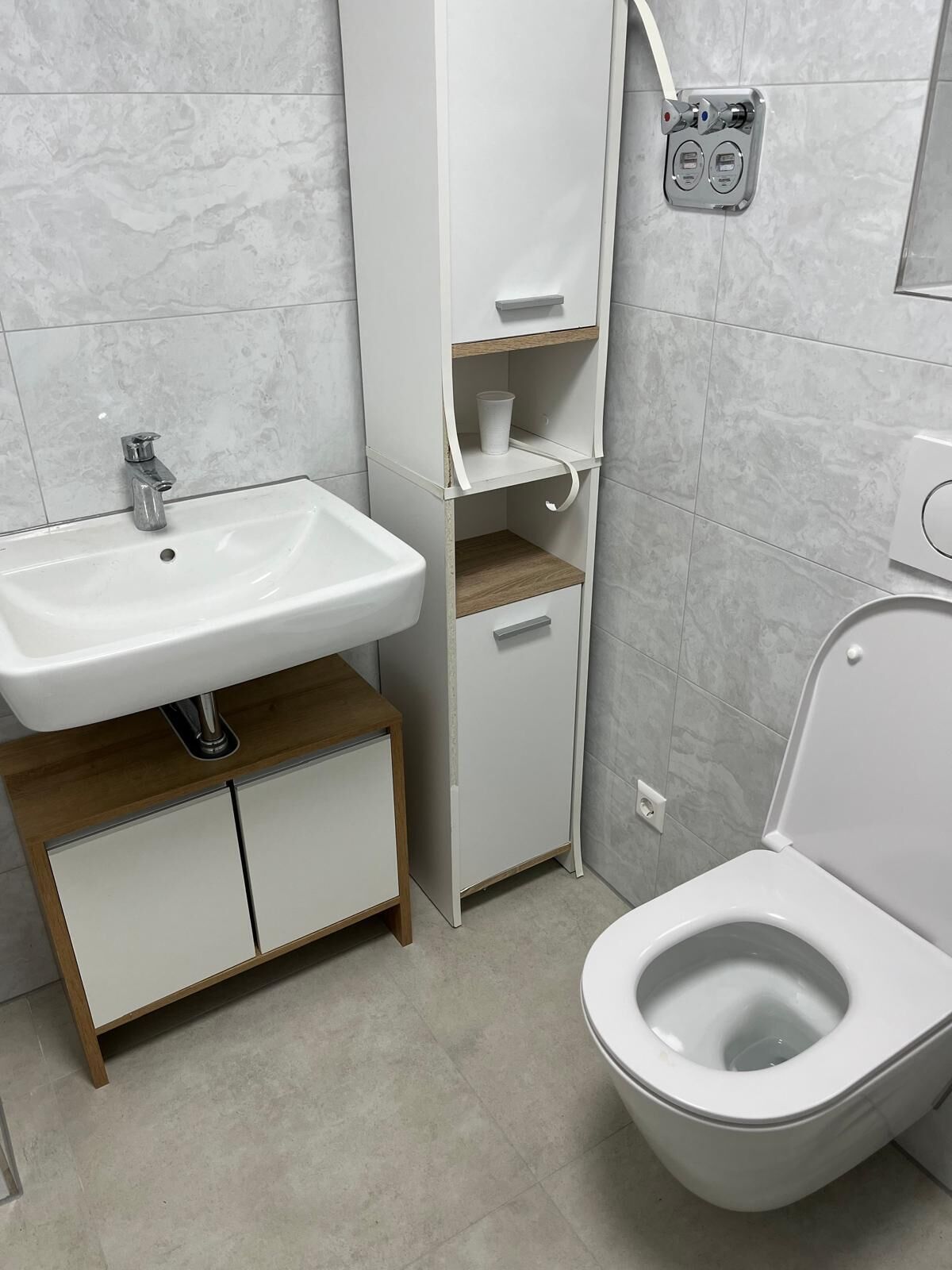 A modern bathroom with a white sink, toilet, and built-in shelves.