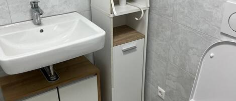 A modern bathroom with a white sink, toilet, and built-in shelves.