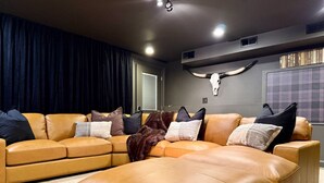 A living room with a tan leather sectional sofa, a large ottoman, and a decorative skull on the wall. - Wild, Wild West Side! Hot tub, Games, Dog Friendly (Conway)