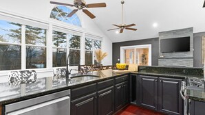 A modern kitchen with dark cabinetry, a granite countertop, and a large window. - Wild, Wild West Side! Hot tub, Games, Dog Friendly (Conway)
