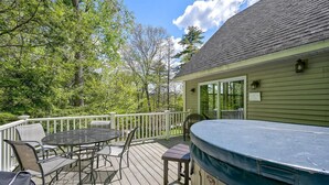 A wooden deck with a hot tub, a table with chairs, and a covered area with a railing.