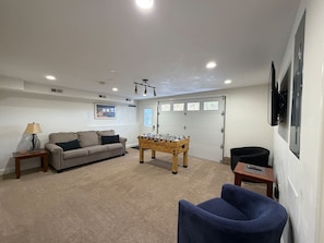 A living room with a sofa, a foosball table, a blue armchair, and a lamp.