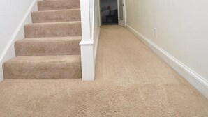 A carpeted staircase with white balusters, leading to a hallway with light-colored walls and a door at the end.
