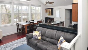 A modern kitchen with a dining area, a gray sofa with decorative pillows, and a ceiling fan.