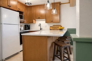A kitchen with wooden cabinets, a white countertop, a built-in stove, a sink, and two hanging pendant lights. - Storybook setting, cozy retreat (Bartlett)