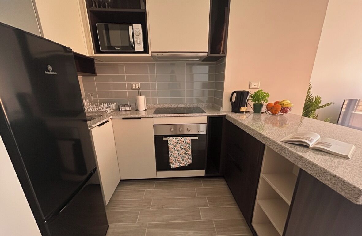 Cocina compacta con refrigerador negro, microondas, estufa y lavamanos. Hay una encimera con un cuenco de fruta y una planta en maceta.