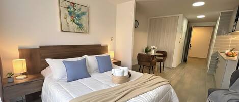 Habitación de hotel con una cama grande, un cabecero de madera, una mesita de noche con lámpara, una pequeña planta en maceta y un cuadro en la pared.
