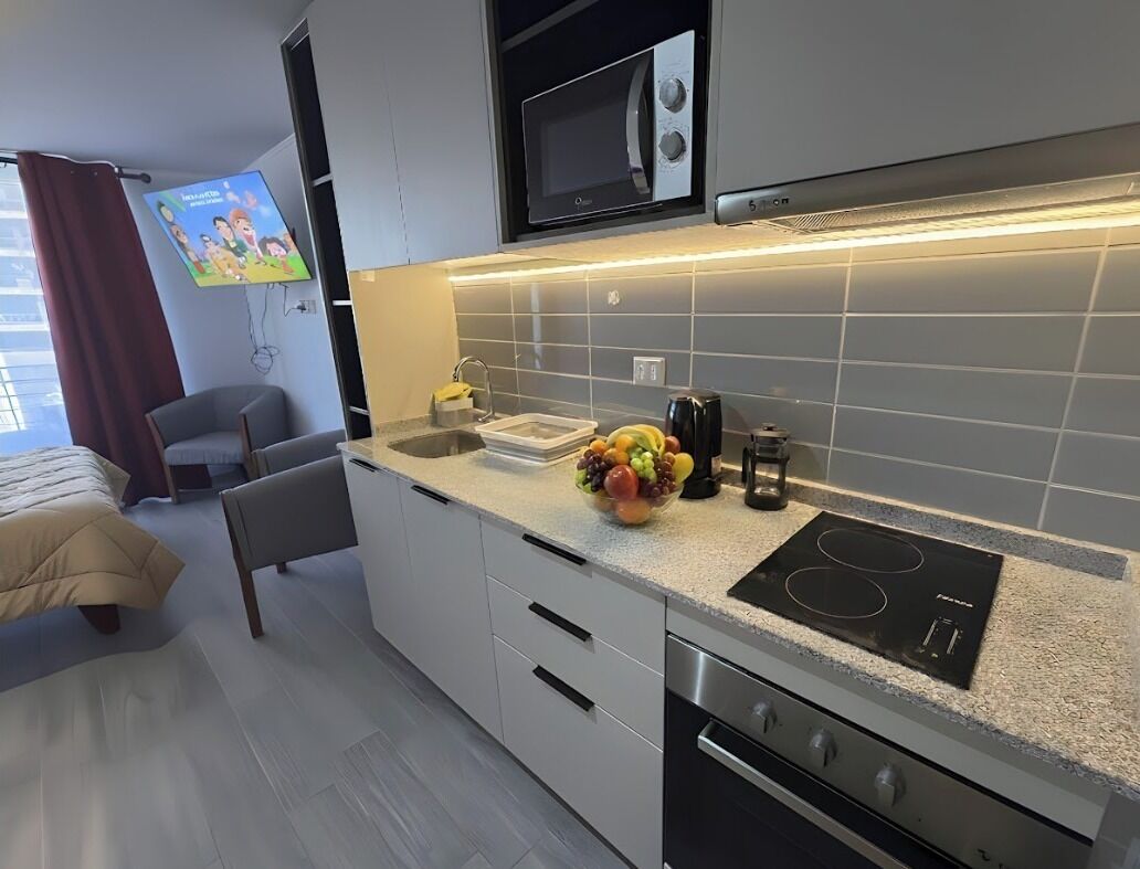 Una cocina moderna con microondas, horno empotrado y un frutero sobre la encimera.