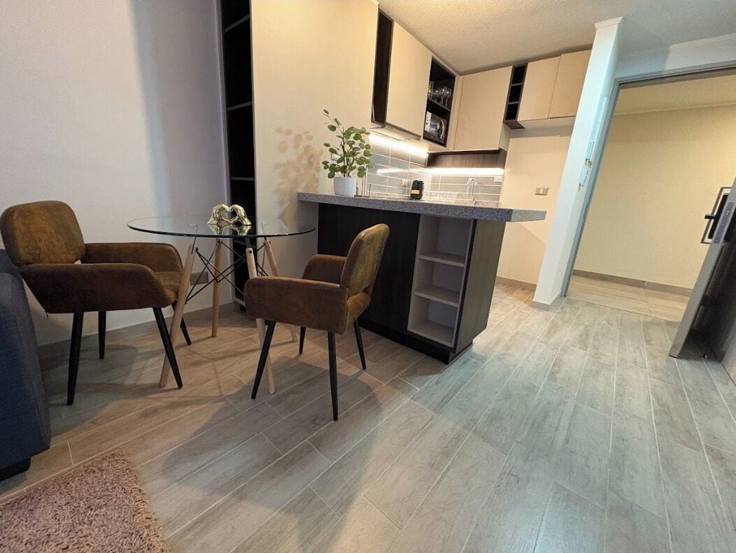 A modern kitchen with a central island, two brown chairs, and a glass table.