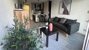 A modern living room with a dark sofa, a coffee table, and a kitchen in the background. - Movistar Arena Santiago - Domus Travels (Santiago)