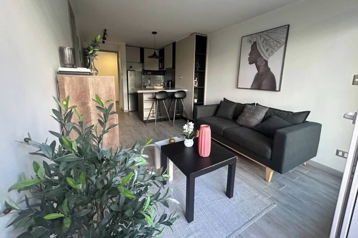 Een moderne woonkamer met een donkere bank, een salontafel en een keuken op de achtergrond.
