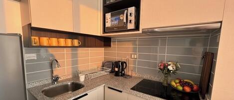 Une cuisine compacte équipée d’un four à micro-ondes encastré, d’une machine à café et d’un panier à fruits posé sur le plan de travail.