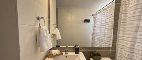 A modern bathroom with a large mirror, white tiles, a sink with a soap dispenser, and a shower curtain.