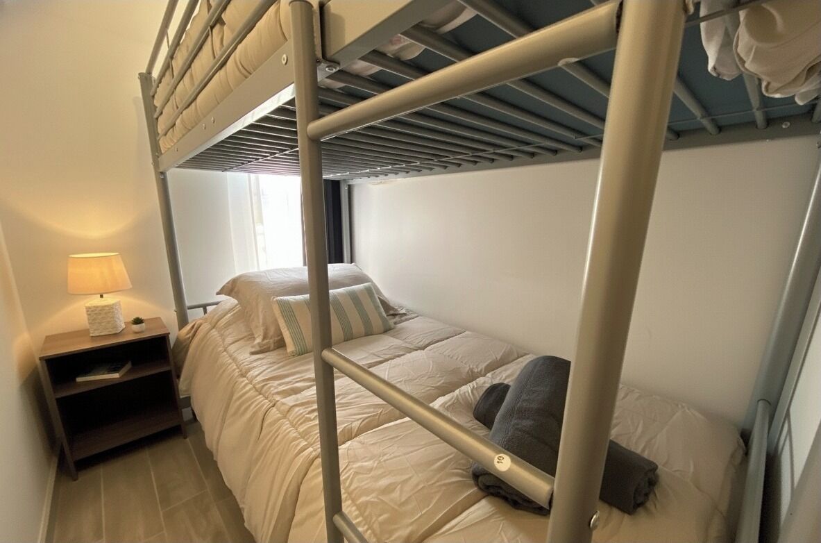 Ein Schlafraum mit Etagenbetten, Nachttisch, Lampe und Fenster.
