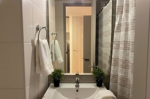 Een badkamer met een wastafel, twee planten in potten, een handdoekrek met handdoeken en een douchegordijn.