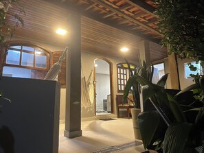Un espacio interior acogedor con vigas de madera en el techo, ventanas amplias y plantas en macetas.