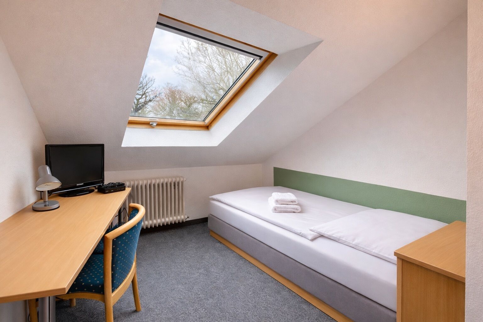 Une petite pièce bien éclairée, avec un bureau, une chaise et un lit.