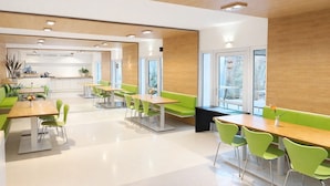 A modern dining area with green chairs and tables, wooden accents, and large windows. - Silvio-Gesell-Tagungsstätte (Wuppertal)