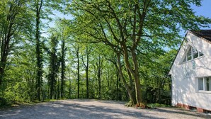 A gravel driveway leading to a white building with a sloped roof, surrounded by a dense forest. - Silvio-Gesell-Tagungsstätte (Wuppertal)