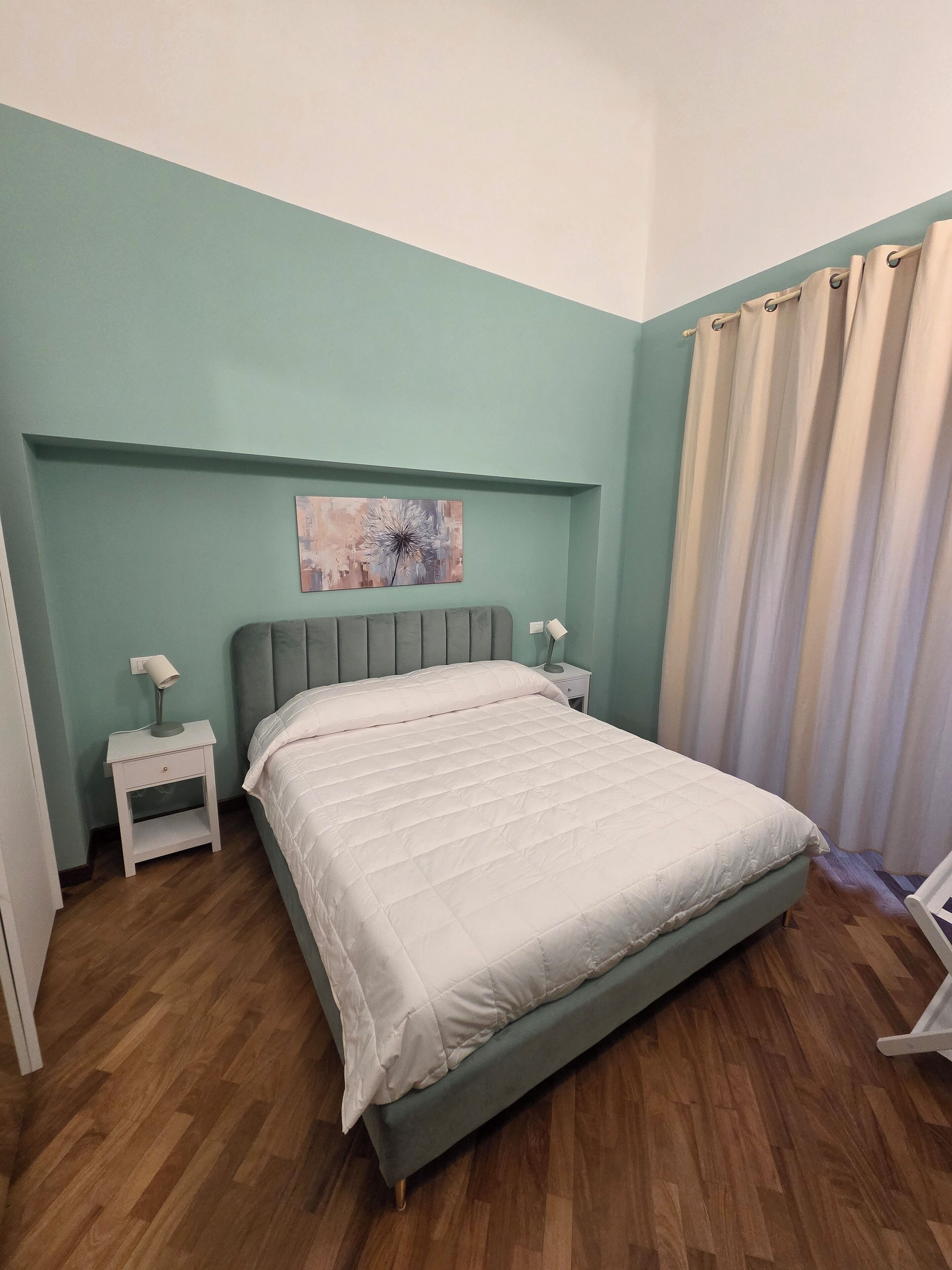 A bedroom with a bed, a nightstand, a lamp, and a painting on the wall.
