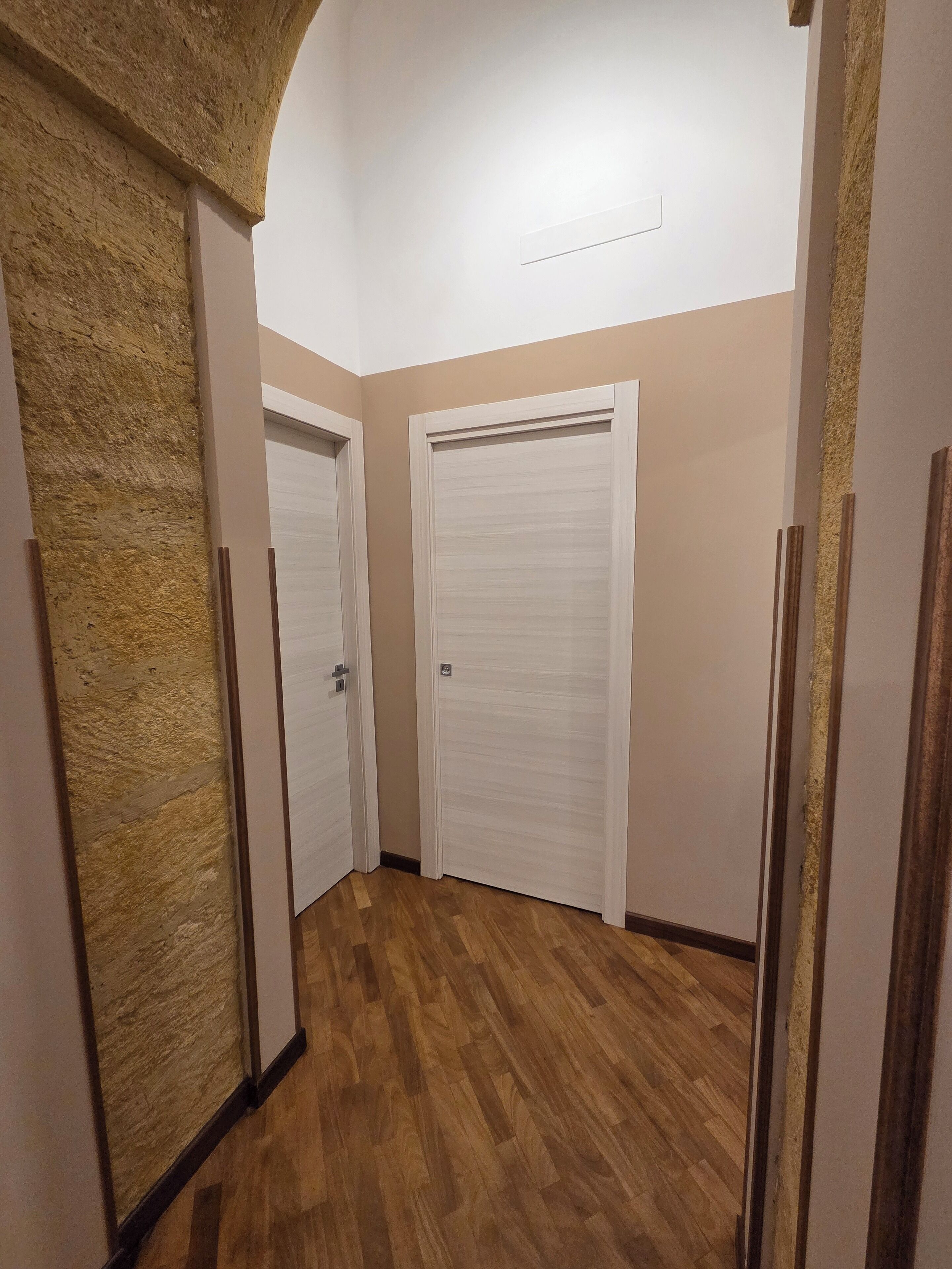 Un pasillo con piso de madera, dos puertas cerradas y paredes con textura.